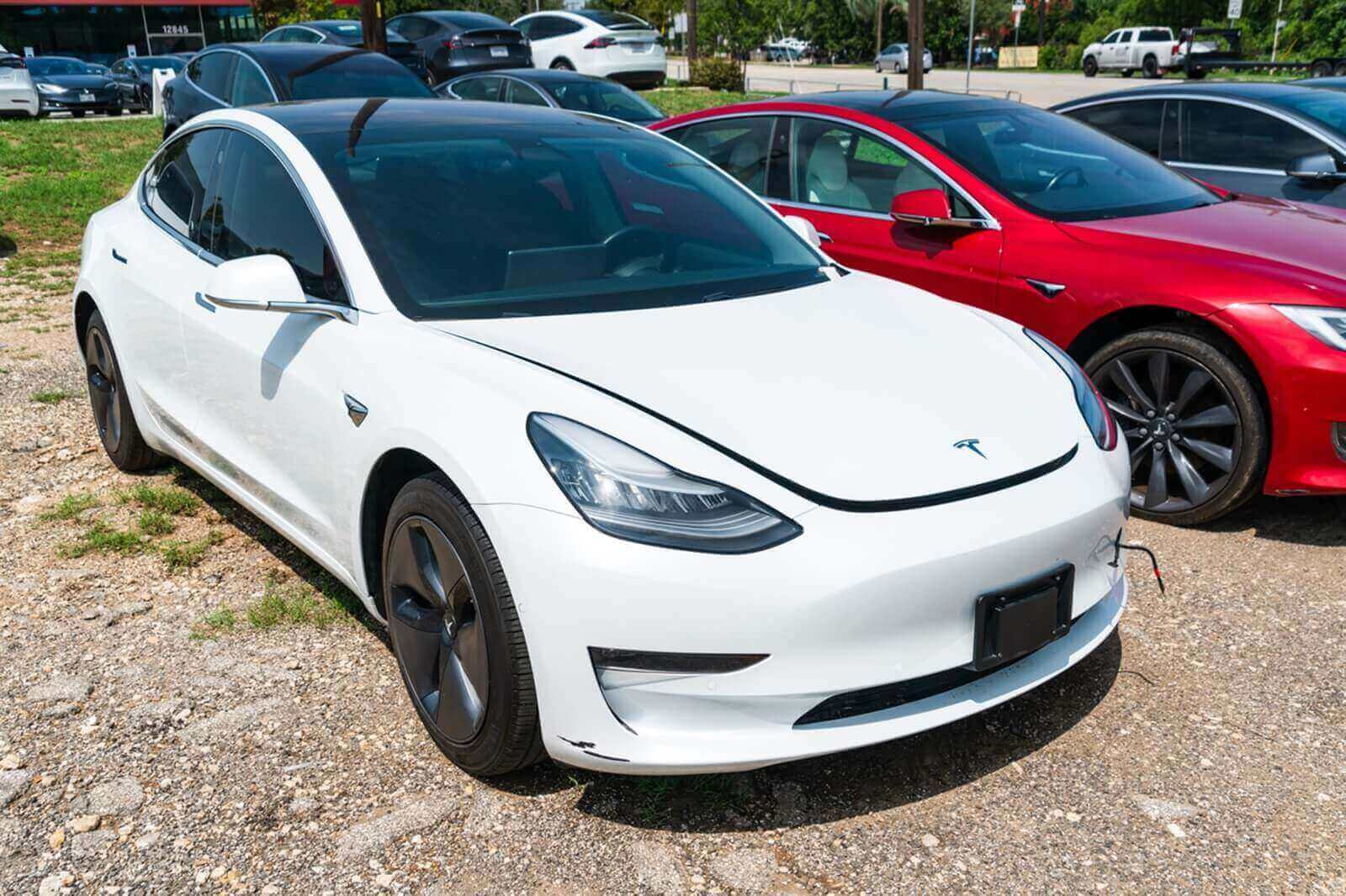 A white Tesla Model 3 shows off its damage in a lot.