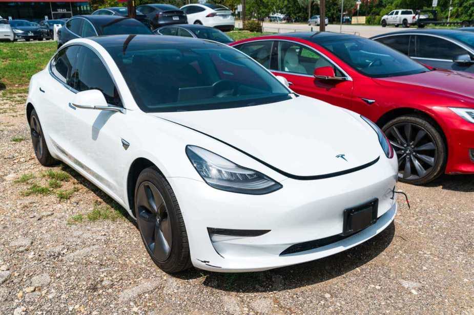 A white Tesla Model 3 shows off its damage in a lot.