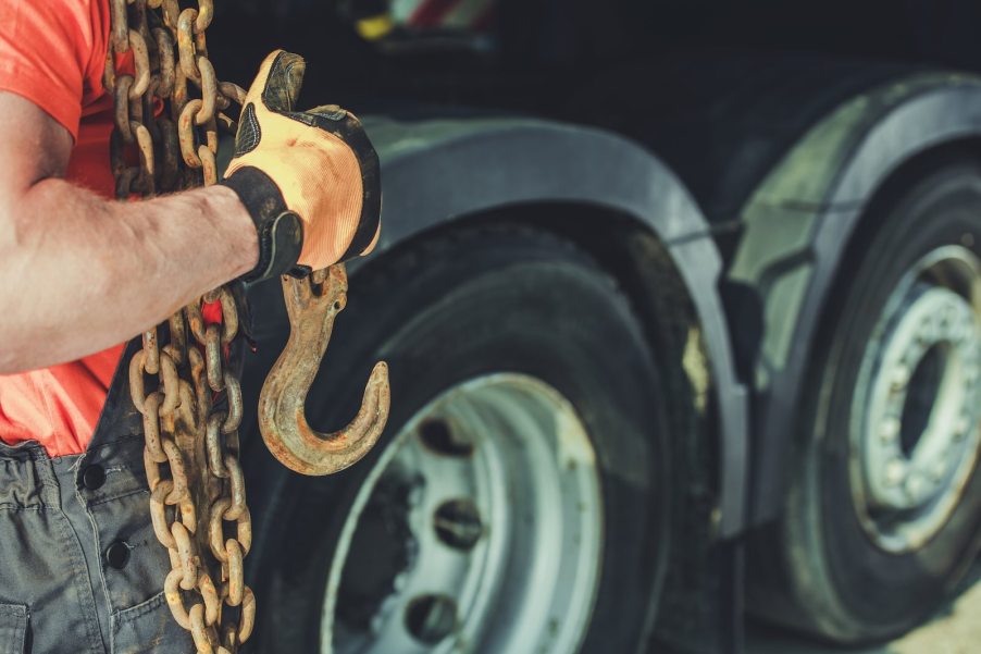 Tow truck driver carrying chains to hook up to a mover work vehicle.