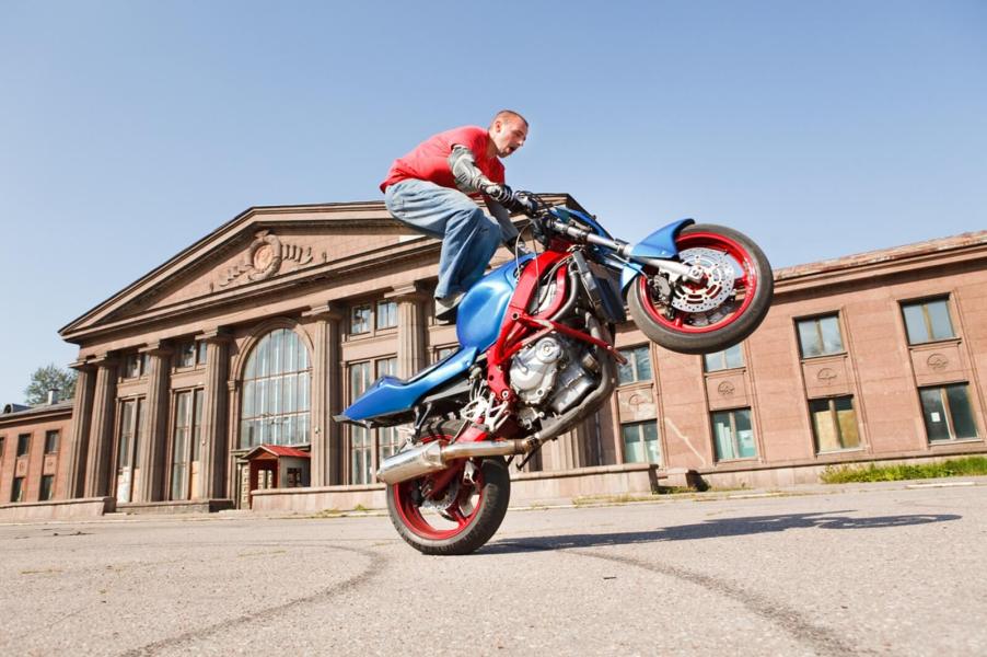A motorcycle rider performing a wheelie in a city square.