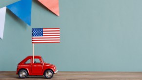 A small American flag positioned on an even smaller red toy car