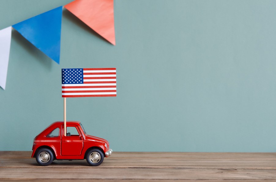 A small American flag positioned on an even smaller red toy car