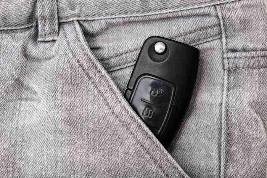 A block car key fob sitting partially in a front pocket of gray denim pants