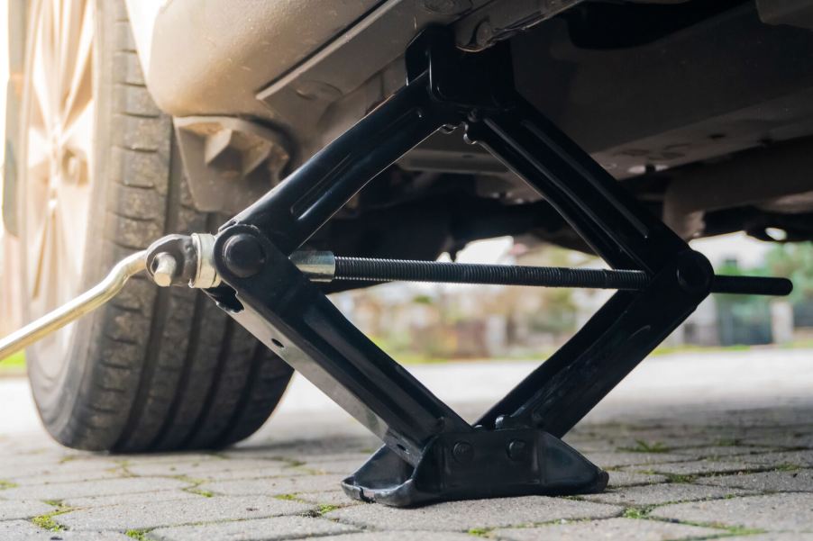 A car scissor jack positioned under a vehicle's left frame rail