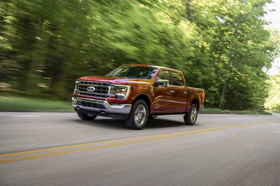 A red Ford F-150 driving on a tree-lined road in left front angle view