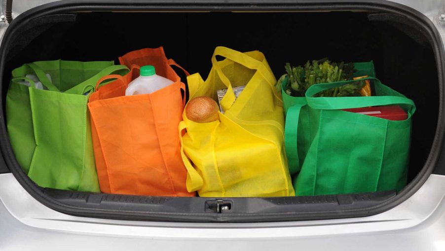 Groceries in reusable bags in an open car trunk