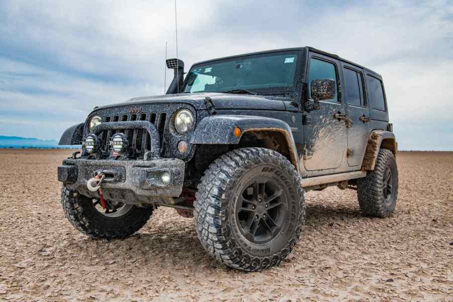 Dark colored Jeep Wrangler with a snorkel parked on desert sands in low left front angle view