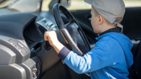 A young boy sitting behind the wheel of an SUV, with his hand on the gear shifter