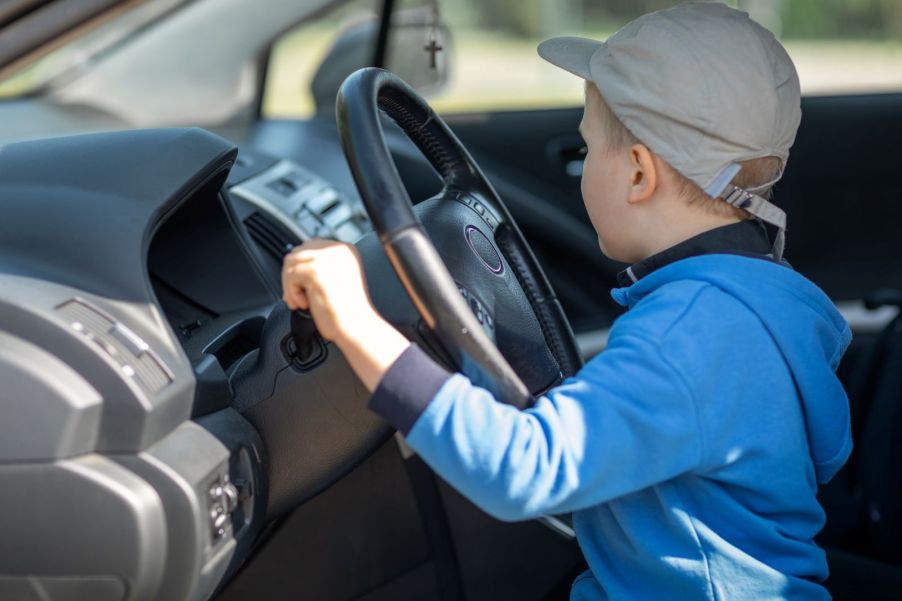 A young boy sitting behind the wheel of an SUV, with his hand on the gear shifter