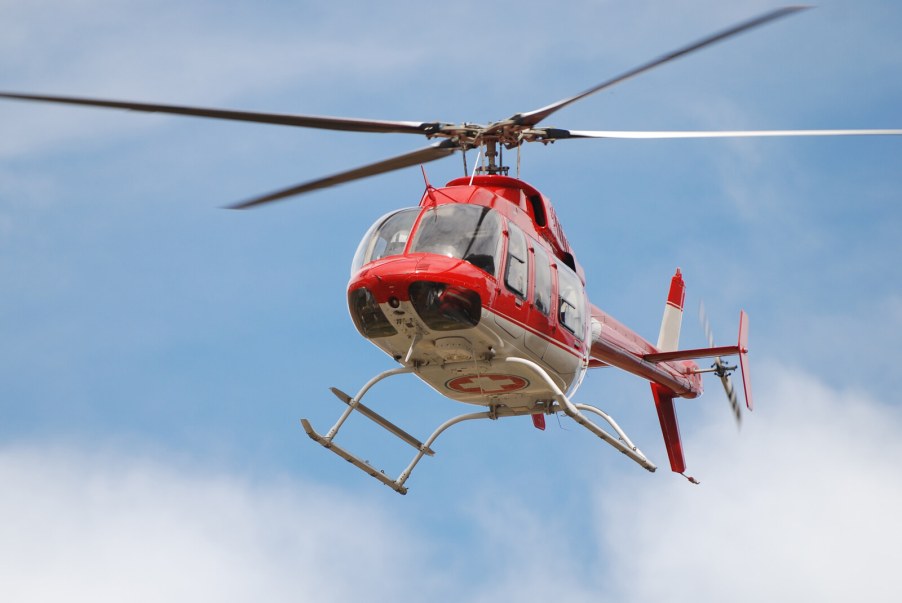A red medical helicopter flying in a cloudy blue sky belly view