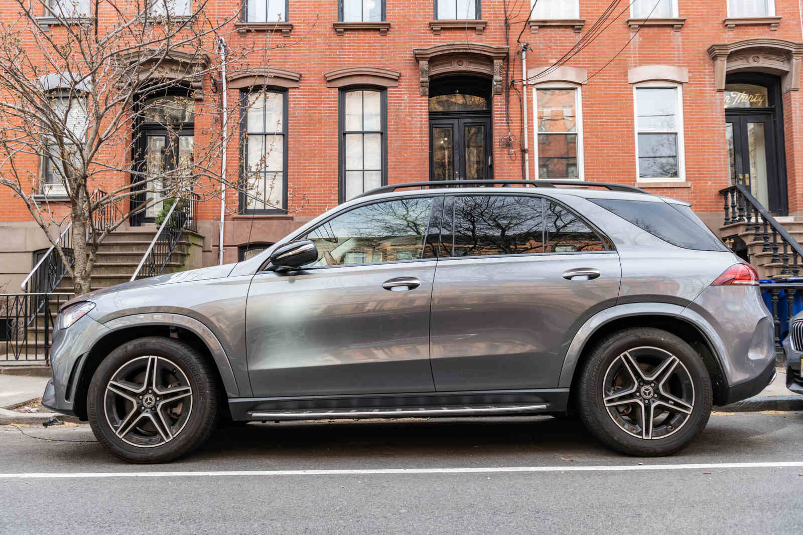A grey metallic Mercedes SUV parallel parked on a residential city street