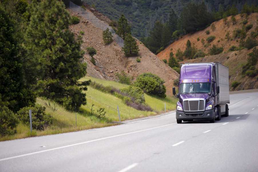 A semi-truck with a purple cabin driving through a California mountain pass