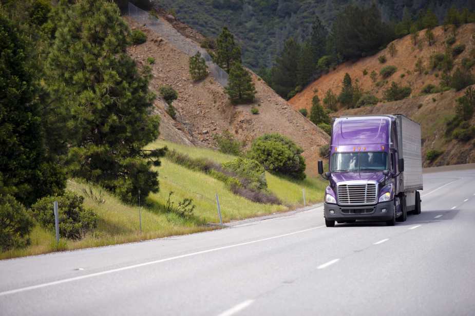 A semi-truck with a purple cabin driving through a California mountain pass