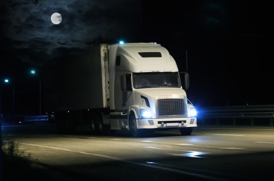 A white semi-truck driving at night with moon in background