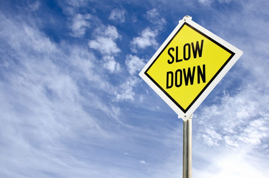 A yellow road sign that reads "SLOW DOWN" against a cloudy blue sky backdrop