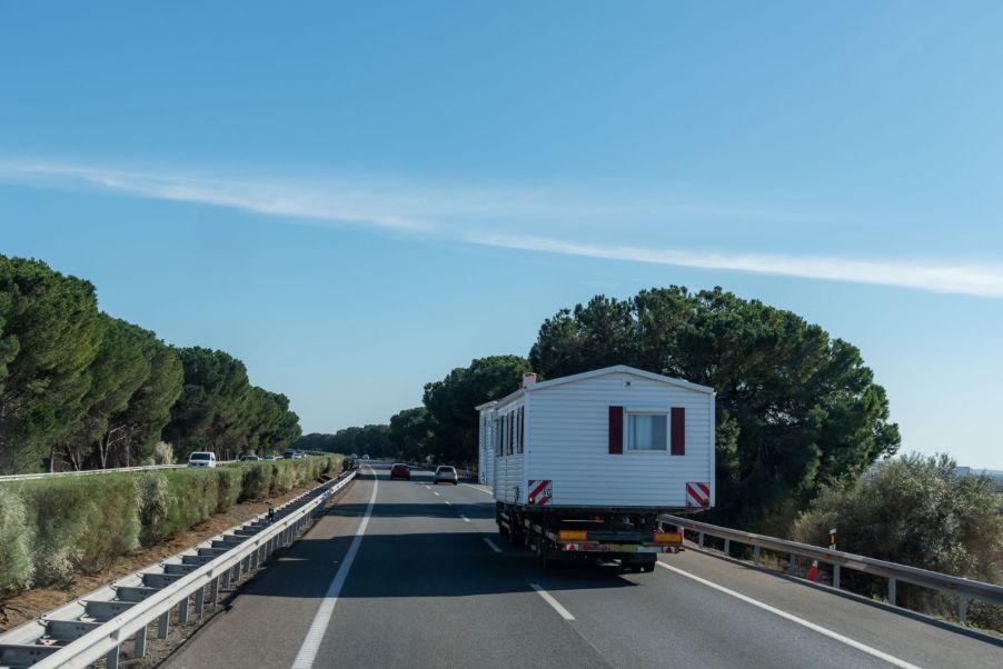 A double wide mobile home traveling down a highway