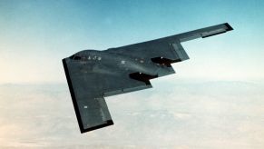 Black B-2 stealth bomber flying a mission, mountains visible below.