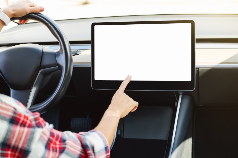 Woman taps a blank, white infotainment screen like those recalled in Cadillac Lyriq and Lincoln Nautilus crossover SUVs