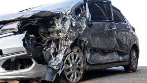 Silver sedan crumpled in underride crash with semi truck trailer guard.