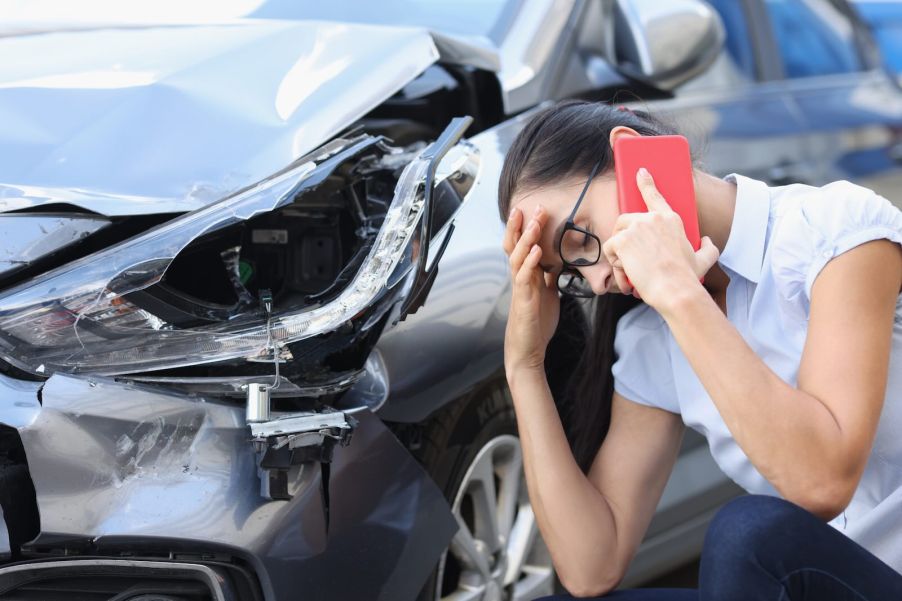 Woman makes a phone call after car crash, smashed vehicle in the background.