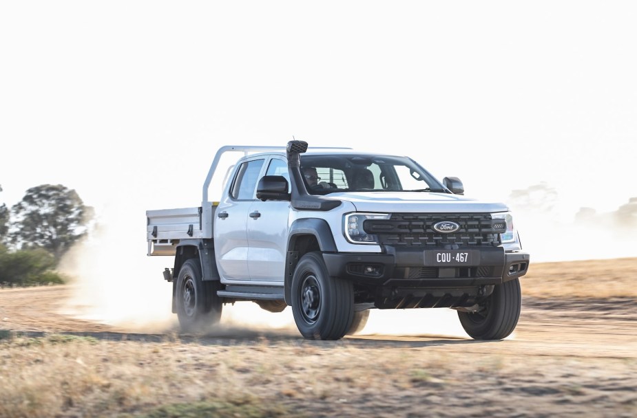 White diesel Ford Ranger Super Duty driving through the outback, dust and trees visible in the background