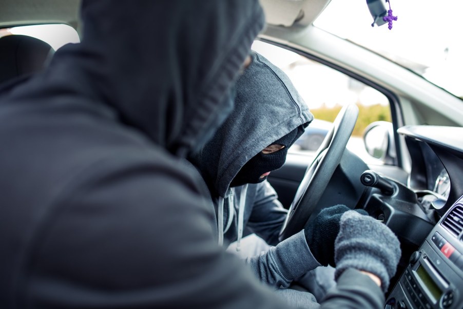 Two car thieves fumble with the ignition of a luxury sports car.