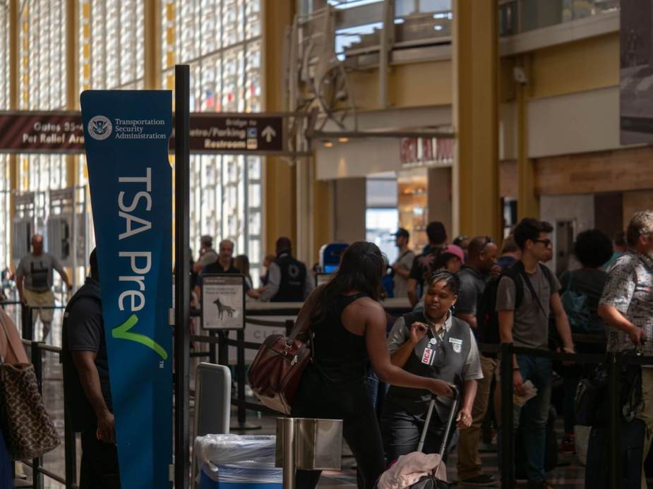 Travelers at a busy TSA checkpoint at a crowded airport.