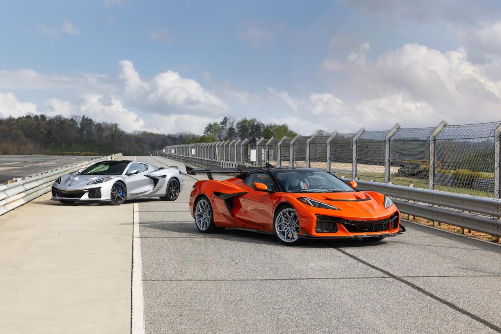 An orange Chevrolet Corvette ZR1X convertible parked in front of a silver coupe, a race track visible in the background.