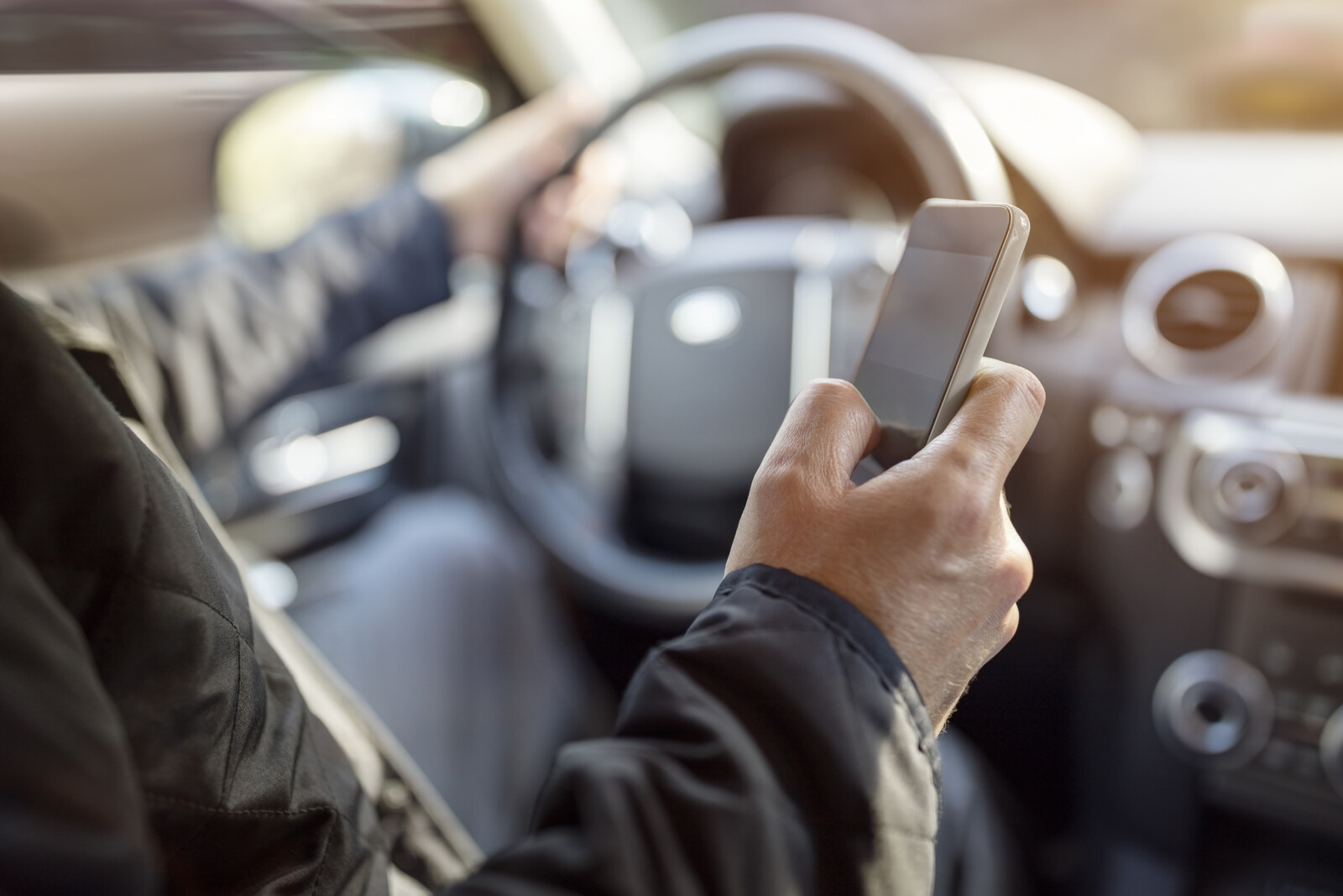 A man's arms shown texting while driving