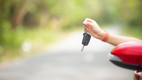 A young person's arm and hand holding a car key out of the window in close view of side mirror