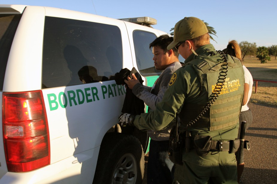 A Border Patrol agent by an SUV stopping a heavy-duty truck