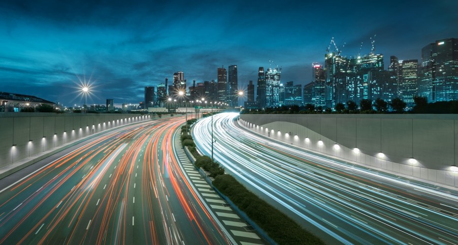 Tail lights of traffic on the highway, Singapore city's skyline visible in the background.