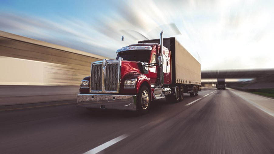 A red semi-truck driving fast on the highway in left front angle view