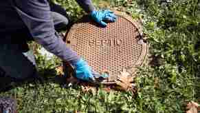 Gloved hands touching a septic system cover on grass