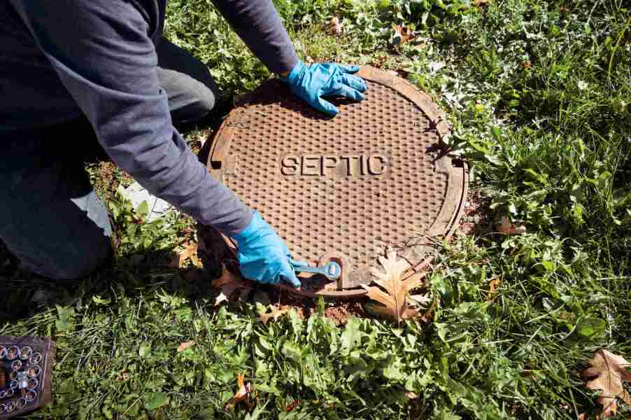 Gloved hands touching a septic system cover on grass