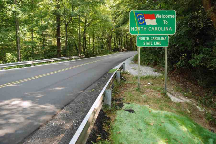 A road sign reading "Welcome to North Carolina" on the side of a wooded road