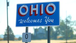 A blue, white, and red road sign reading "Ohio Welcome You"