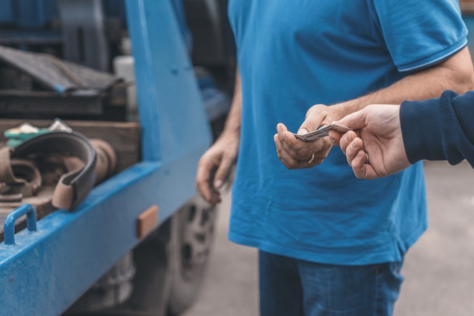 Car owner hands a wad of money to a tow truck driver for storage fees.