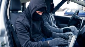 Men in masks use a laptop for car theft