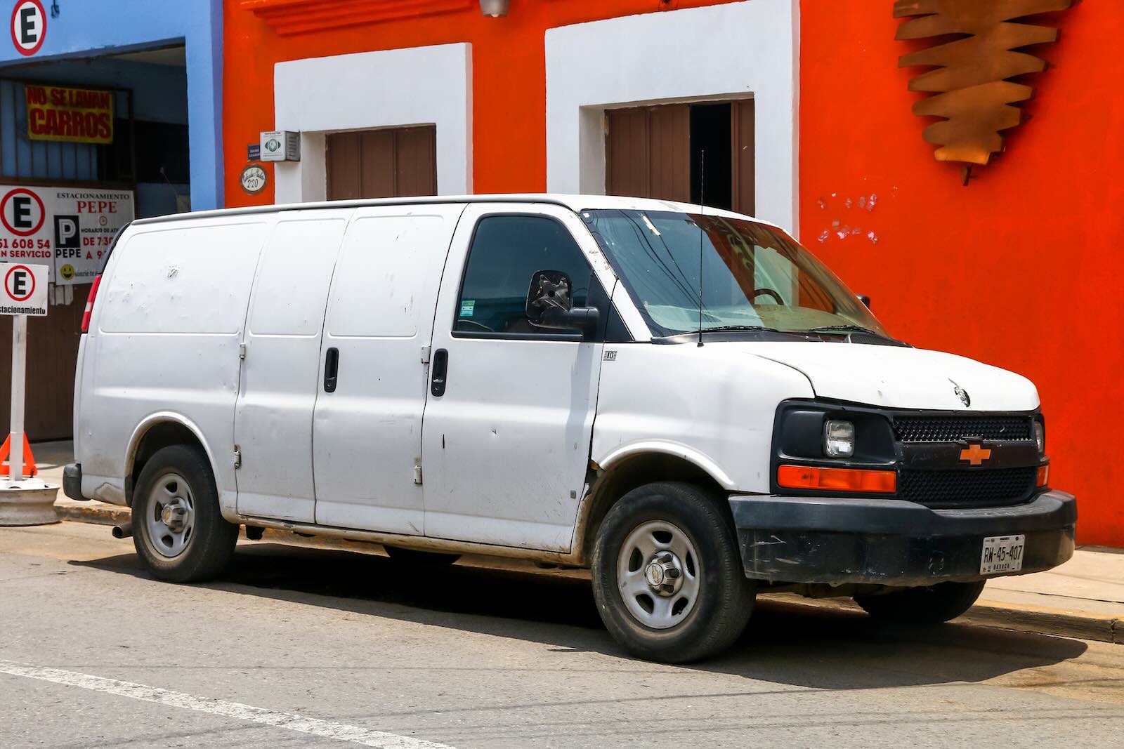 White Chevy Express work cargo van parked on the street in Mexico, colorful buildings in the background