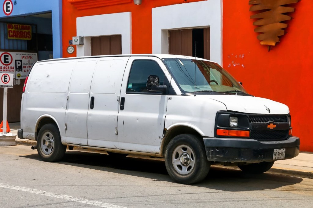 White Chevy Express work cargo van parked on the street in Mexico, colorful buildings in the background