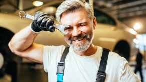 Smiling mechanic winks through a wrench, the auto shop visible in the background.