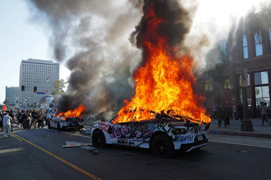 Flames erupt from the top of two Waymo self-driving taxis destroyed by California mob.