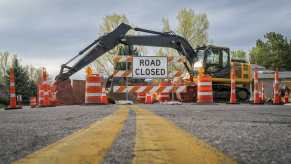 Orange barrels lined up in front of "road closed" sign in front of a backhoe
