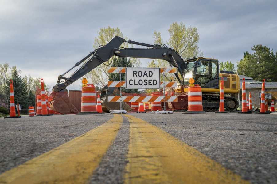 Orange barrels lined up in front of "road closed" sign in front of a backhoe