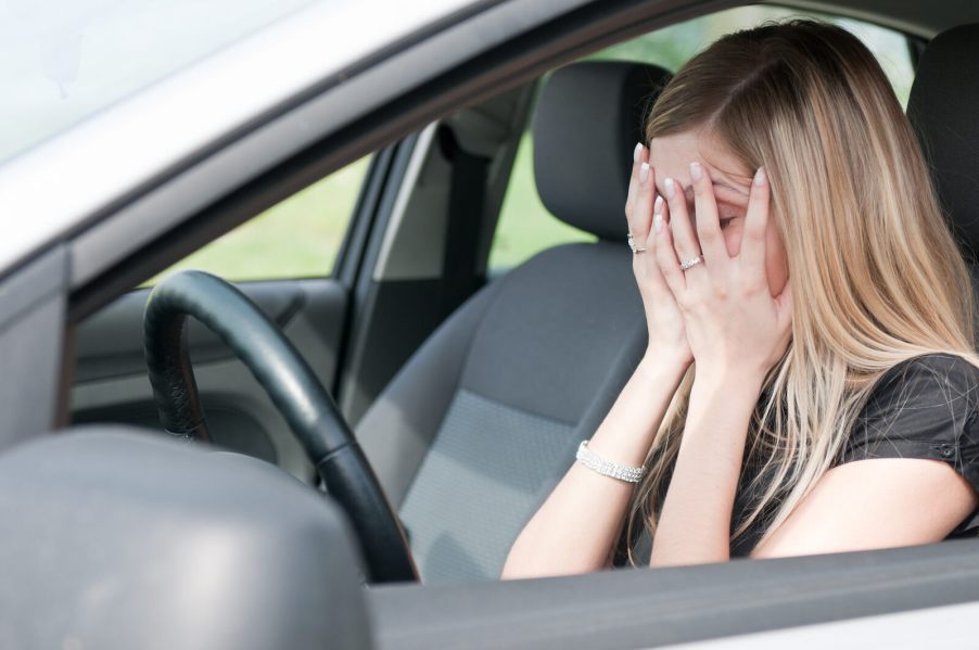 A woman sitting in a car covering her face in frustration