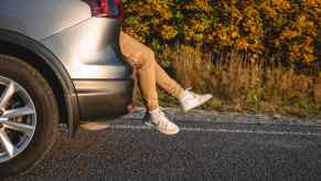 Passenger's legs stick out of SUV with ample legroom, its hatch opened and parked on a country road.