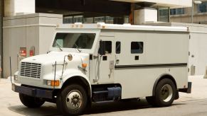 Tan armored truck parked on a sidewalk in front of a building.