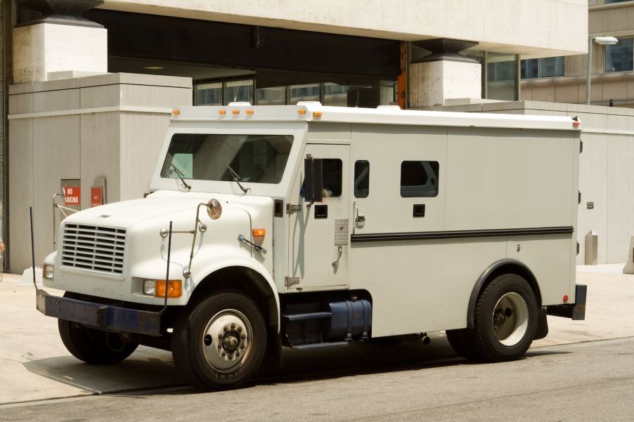Tan armored truck parked on a sidewalk in front of a building.