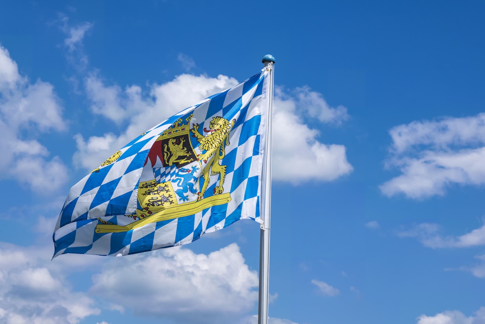 The blue and white Bayern flag of Germany's Bavaria state, in front of a blue sky